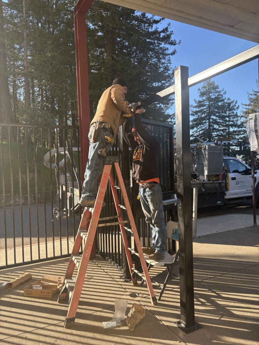 SECURITY OR PRISON? Two workers install doors to a new fence near the Skyline theater on Jan.14. More fencing will be installed over Spring Break.
